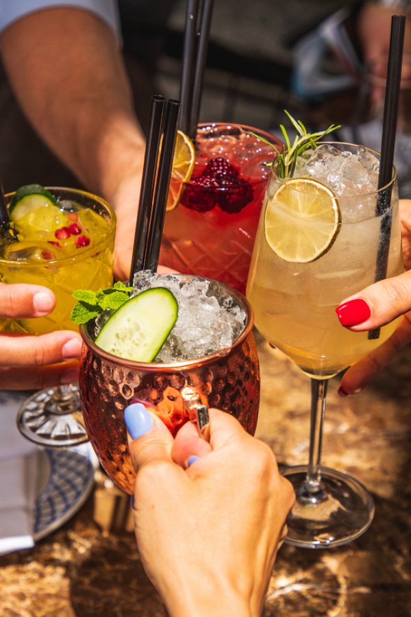 4 Freunde greifen nach Ihrem Glas bei einem Cocktail Tasting in Berlin.